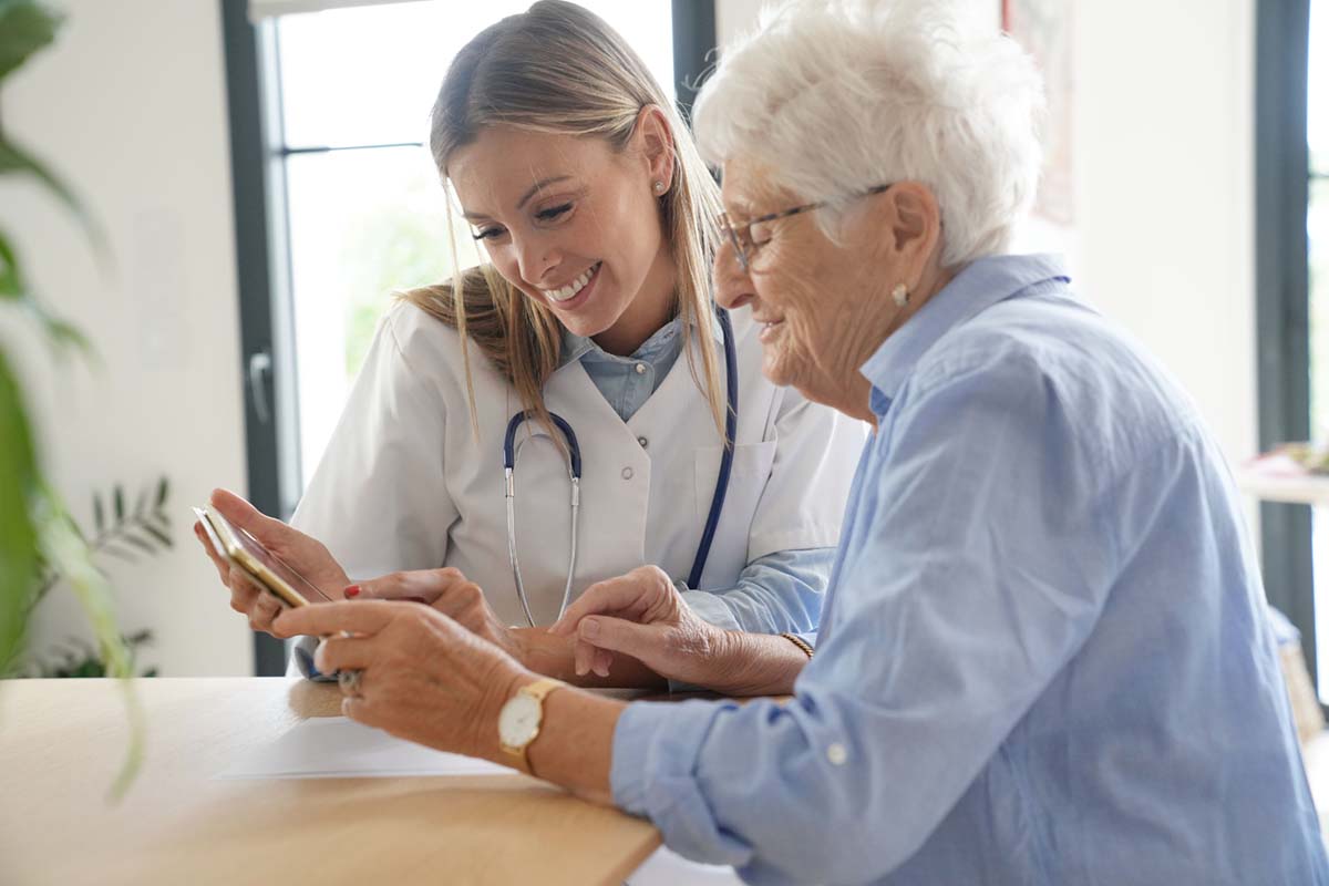 Jasmine Estates of Oklahoma City Dementia Care | Elderly woman with nurse at home looking at tablet